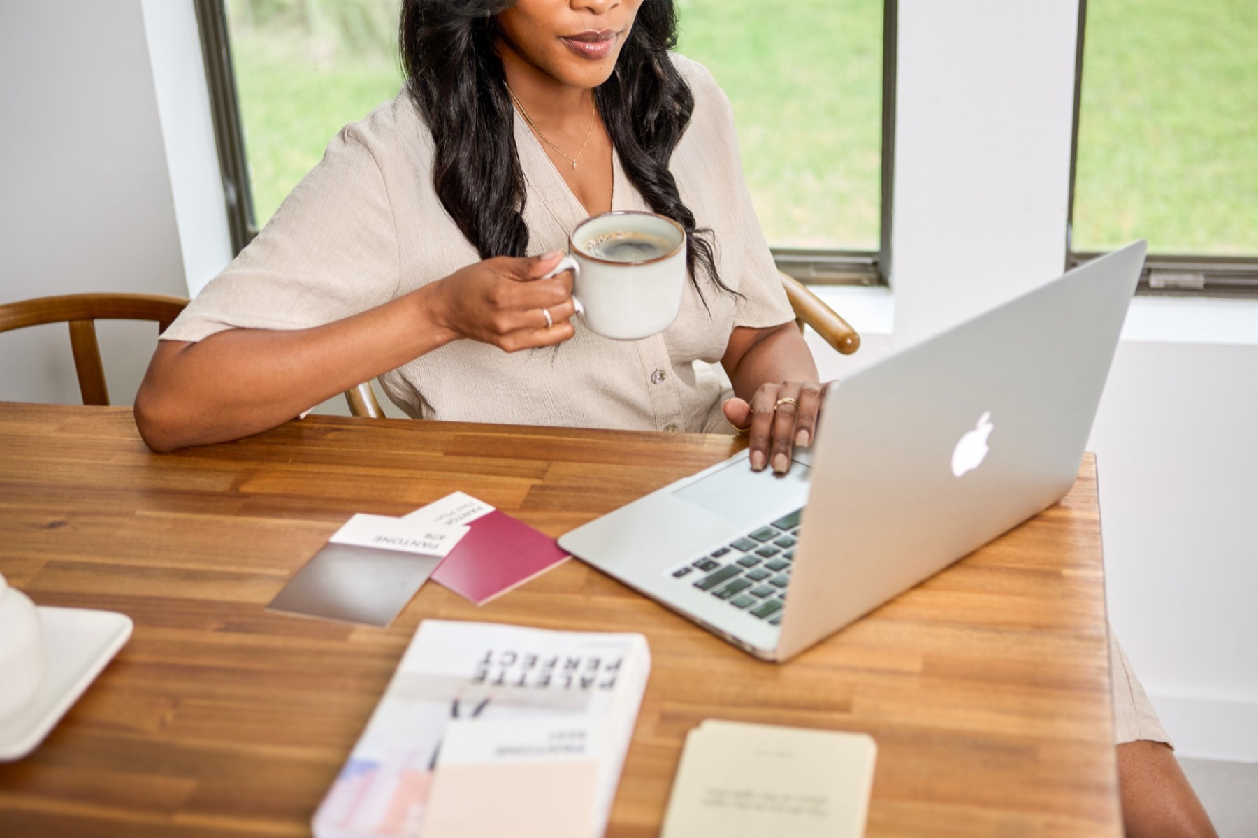 Megan Noel with a cup of coffee, working on her laptop beside color swatches