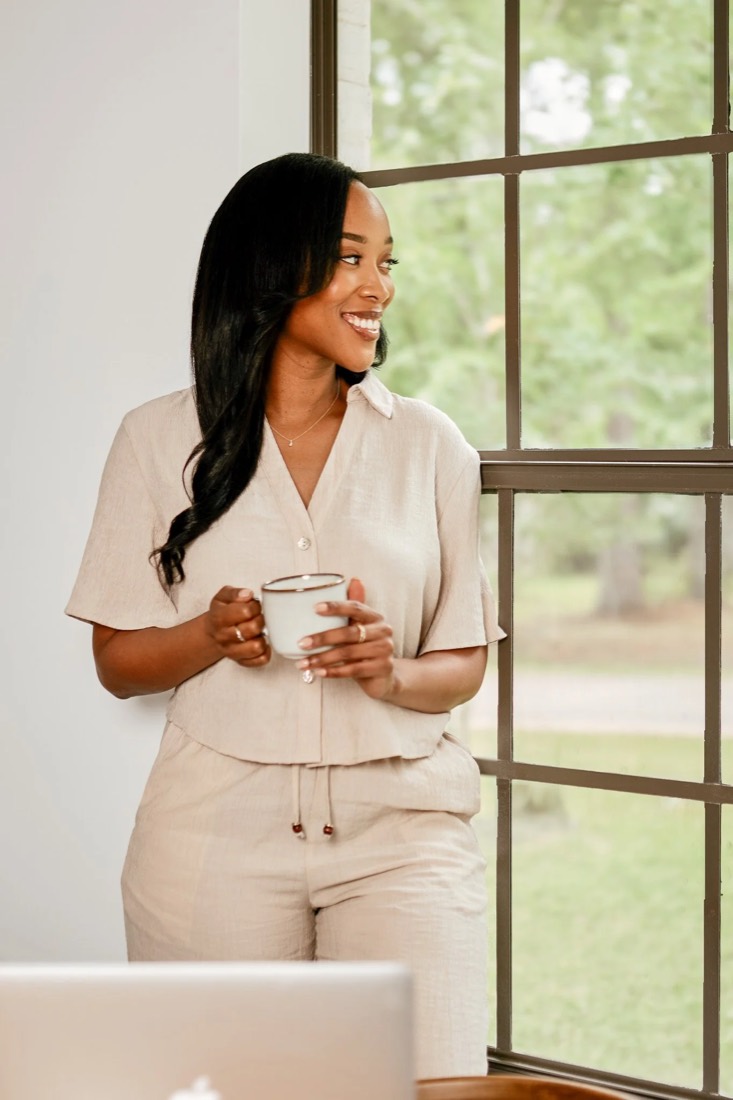 Megan Noel smiling by a window with a cup of coffee